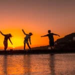 Three friends in the orange sunset on the salt flats and in the background the Fuencaliente Lighthouse on the route of the volcanoes south of the island of La Palma, Canary Islands, Spain